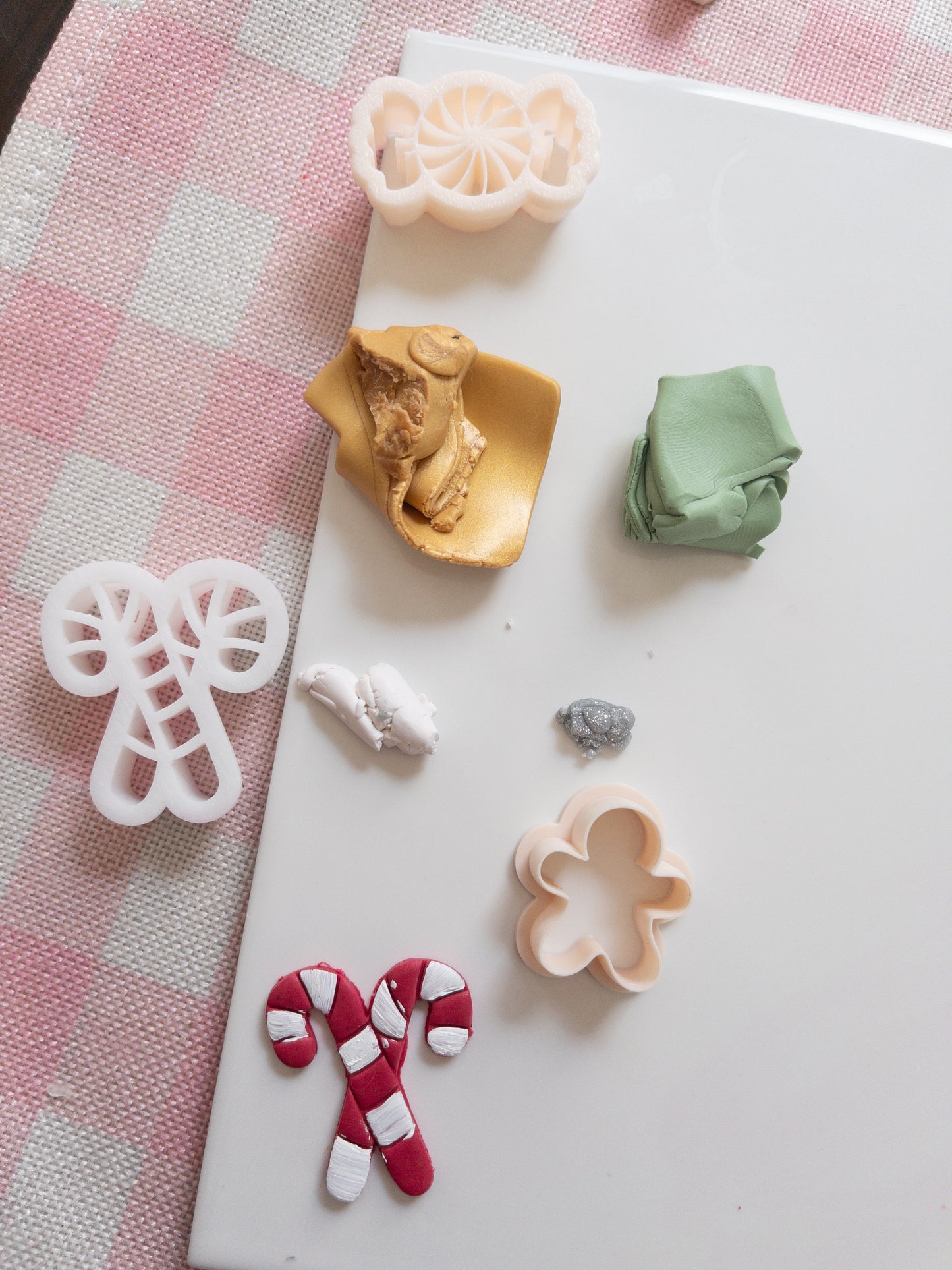 Set of colourful clay and clay cutters on a white surface with a pink checkered fabric background.