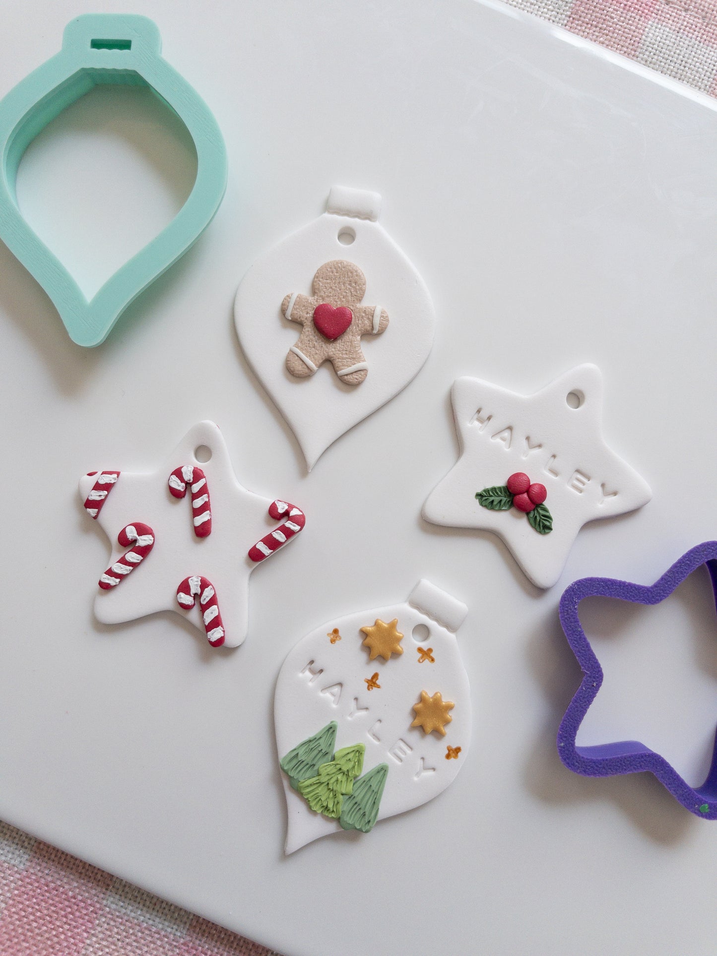Decorative clay ornaments shaped like stars, hearts, and gingerbread men with cookie cutters on a white surface.