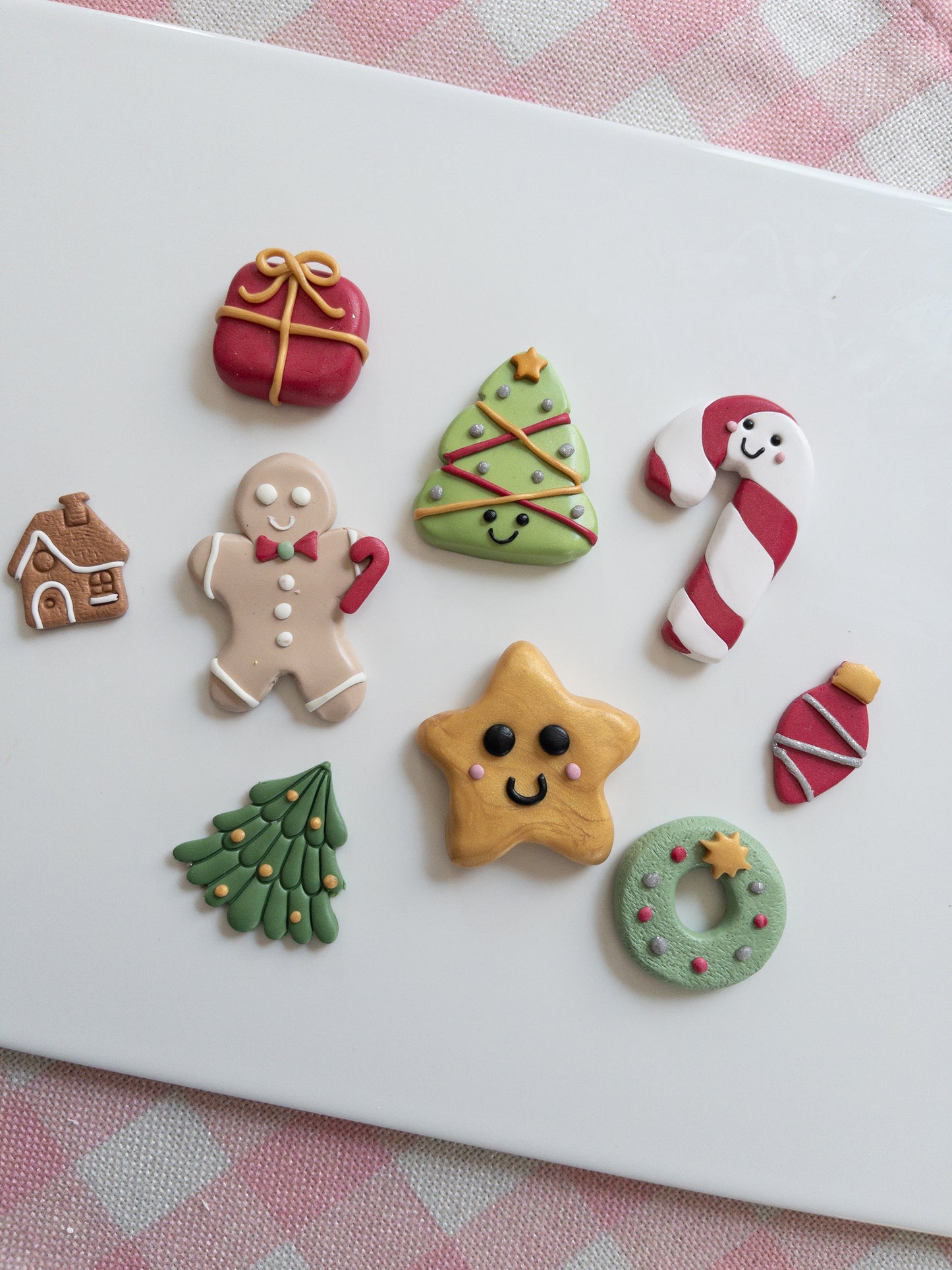 Set of colorful Christmas-themed clay creations on a white surface with a pink checkered background