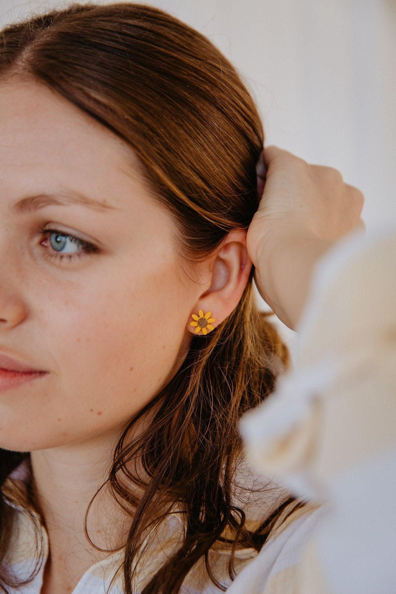 Woman with long brown hair wearing a pair of small sunflower stud earrings