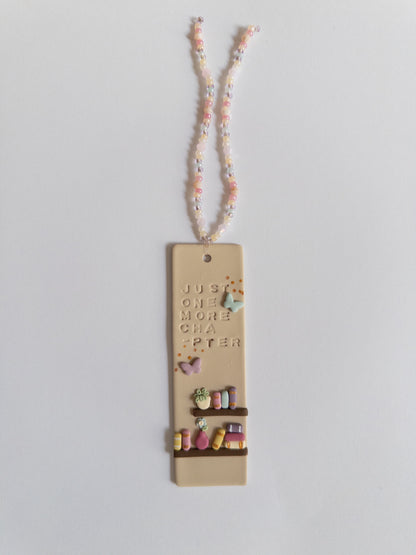 Bookmark with a bookshelf design, and the words 'just one more chapter', with matching beaded tassel on a white background