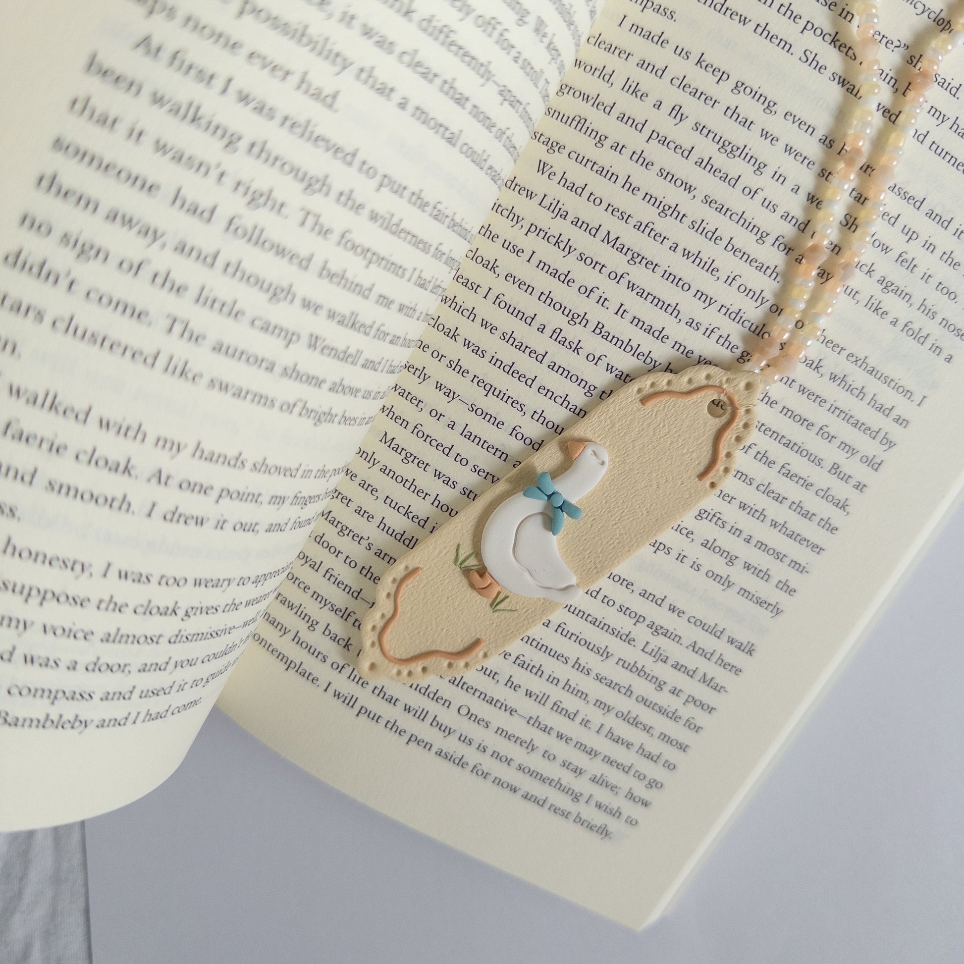 Polymer clay bookmark with a white goose on it on top of an open page of a book
