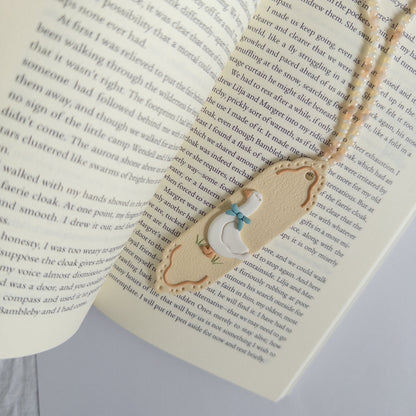 Polymer clay bookmark with a white goose on it on top of an open page of a book