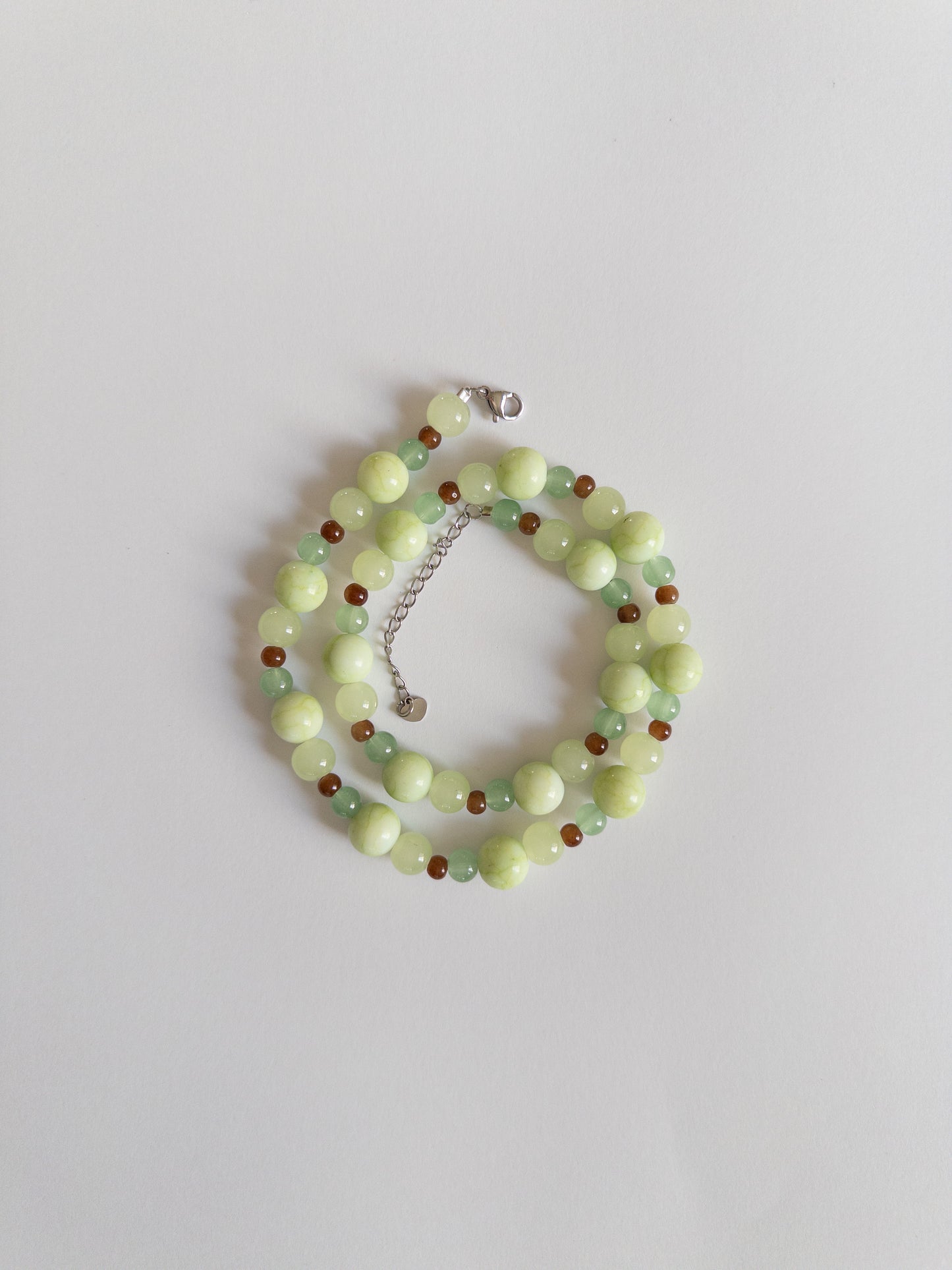 Green and brown beaded necklace styled on a white background