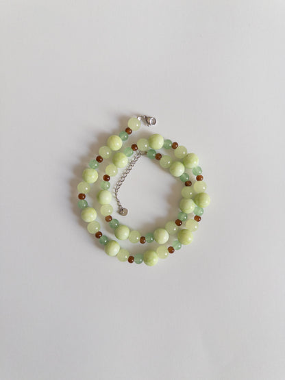 Green and brown beaded necklace styled on a white background