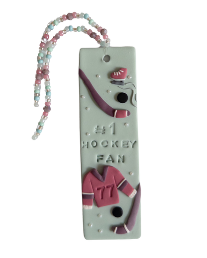 Polymer clay bookmark and matching beaded tassel on white background. Bookmark features a design with the words '#1 Hockey Fan" and hockey sticks and jersey design details