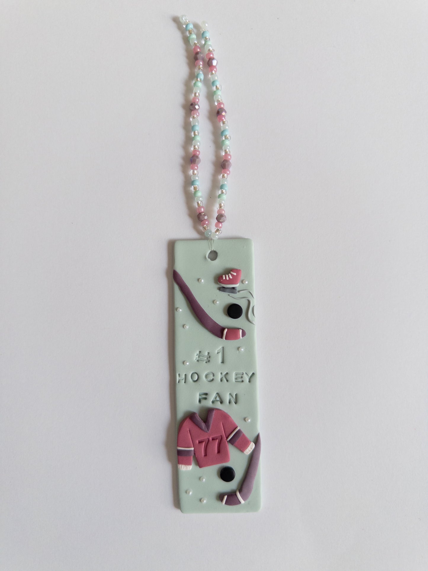 Polymer clay bookmark and matching beaded tassel on white background. Bookmark features a design with the words '#1 Hockey Fan" and hockey sticks and jersey design details
