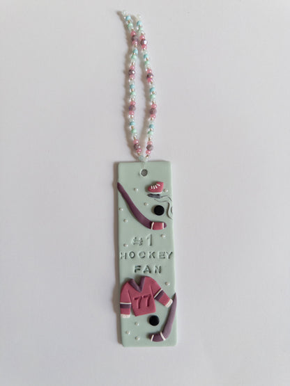 Polymer clay bookmark and matching beaded tassel on white background. Bookmark features a design with the words '#1 Hockey Fan" and hockey sticks and jersey design details