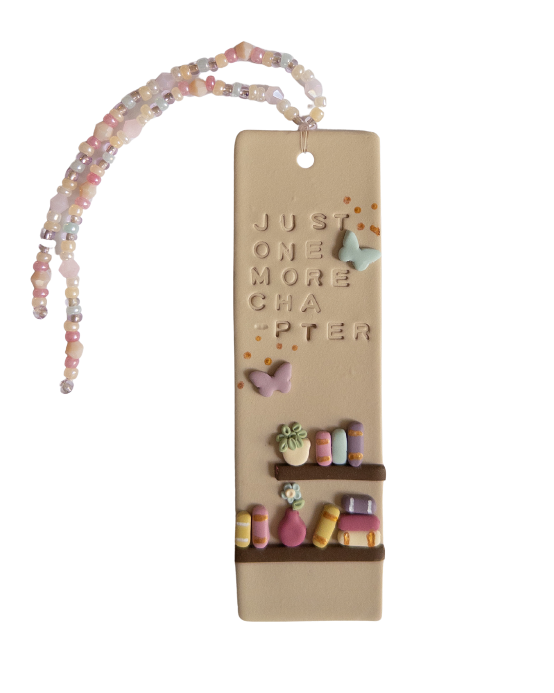 Bookmark with a bookshelf design, and the words 'just one more chapter', with matching beaded tassel on a white background