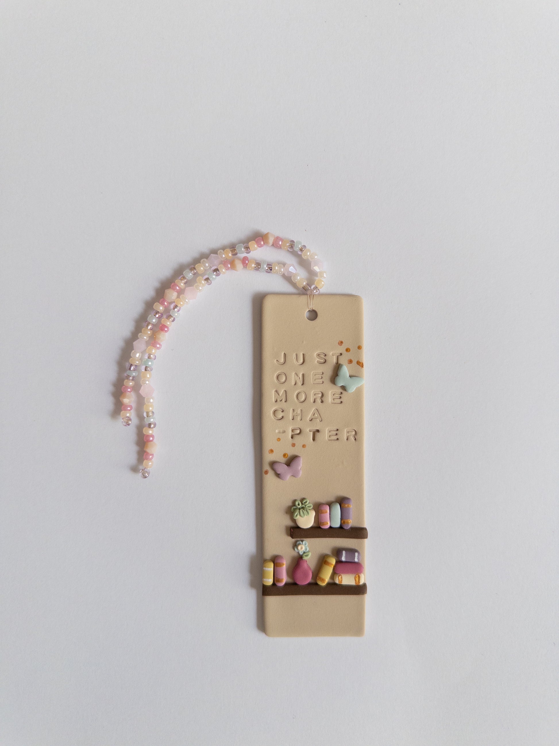 Bookmark with a bookshelf design, and the words 'just one more chapter', with matching beaded tassel on a white background