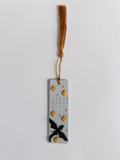Grey polymer clay bookmark with gold coloured tassel on white background. Bookmark features a dragon, gold stars and the words 'live Manon live'
