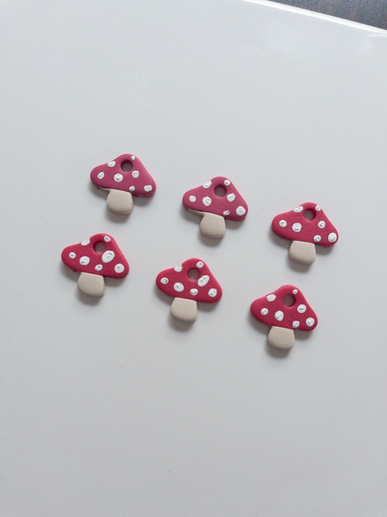 Five pink mushroom-shaped charms with white spots on a light gray background