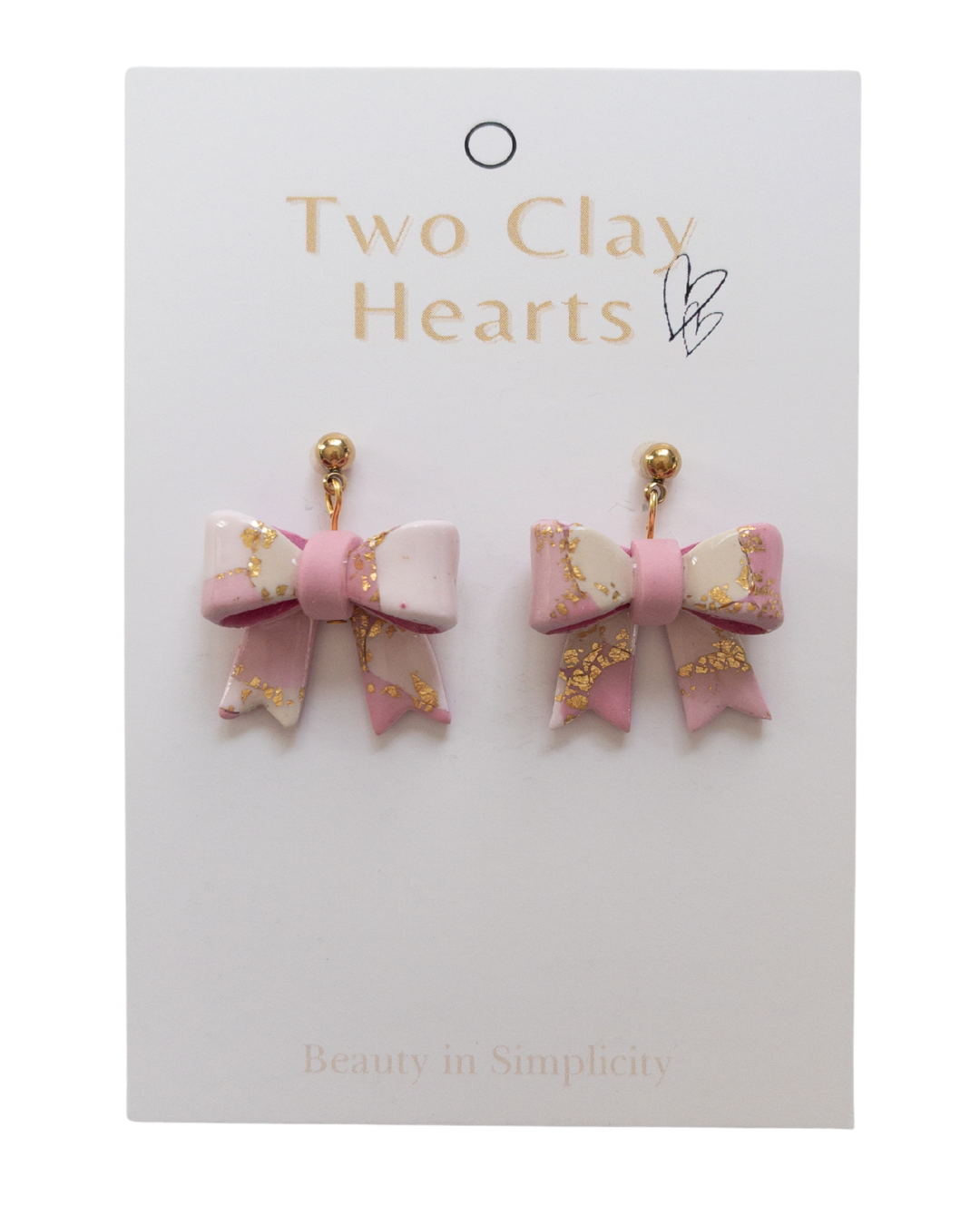 Pink bow-shaped earrings on a 'Two Clay Hearts' branded card.