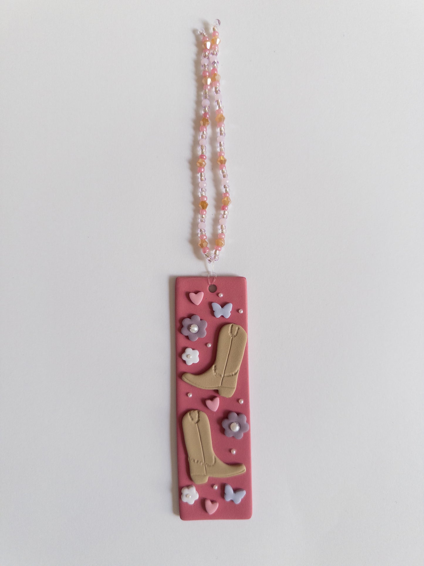 Polymer clay bookmark with a pink background and decorated with brown cowboy boots, purple flowers and butterflies and pink hearts and a matching beaded tassel