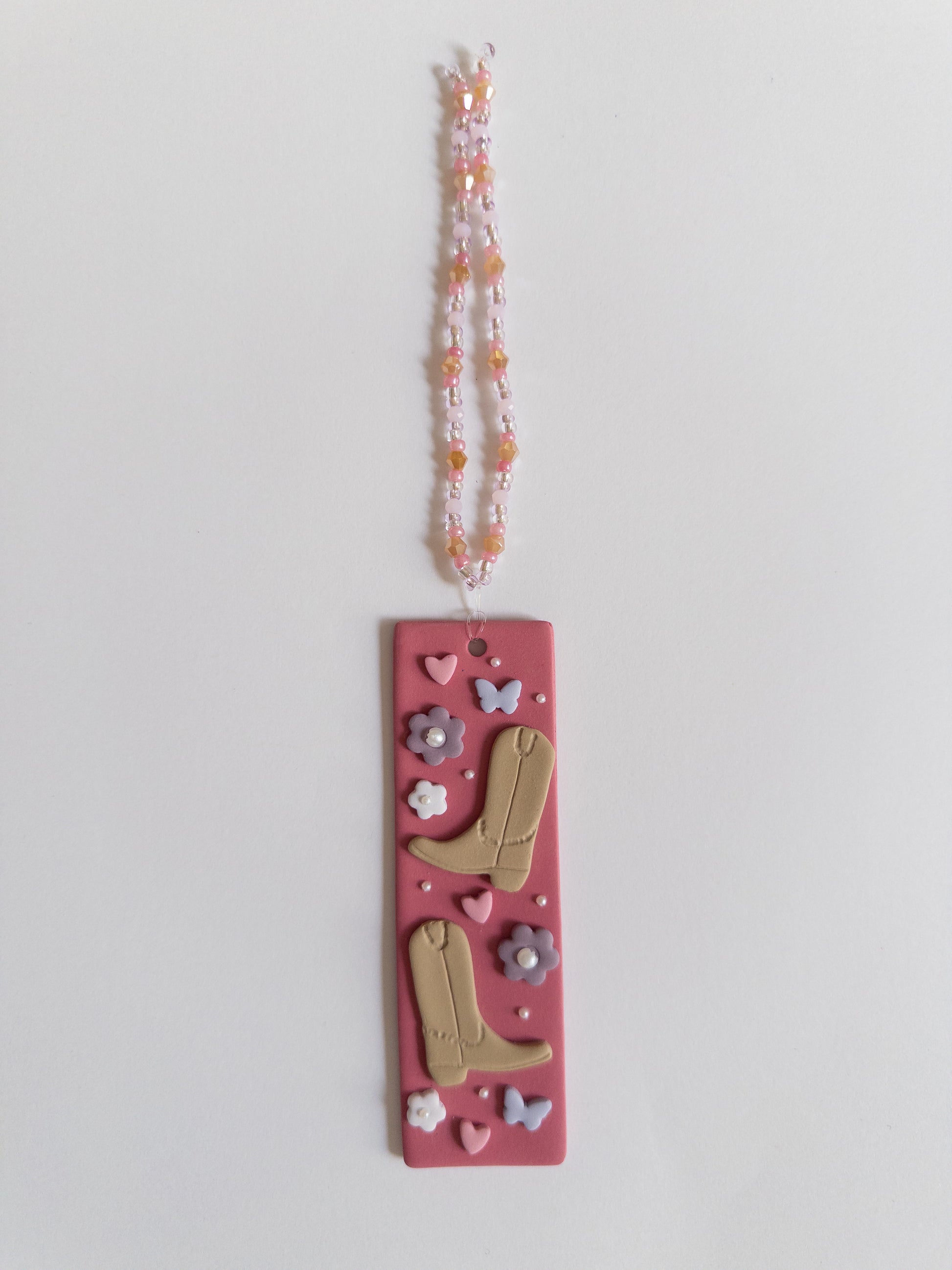 Polymer clay bookmark with a pink background and decorated with brown cowboy boots, purple flowers and butterflies and pink hearts and a matching beaded tassel