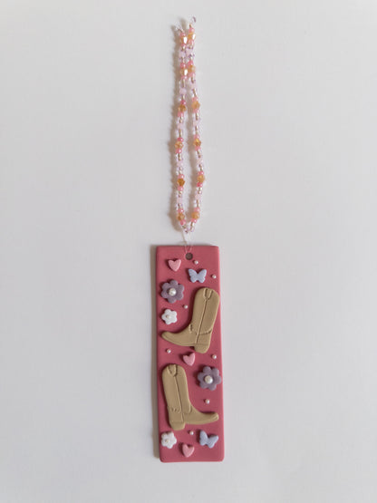 Polymer clay bookmark with a pink background and decorated with brown cowboy boots, purple flowers and butterflies and pink hearts and a matching beaded tassel