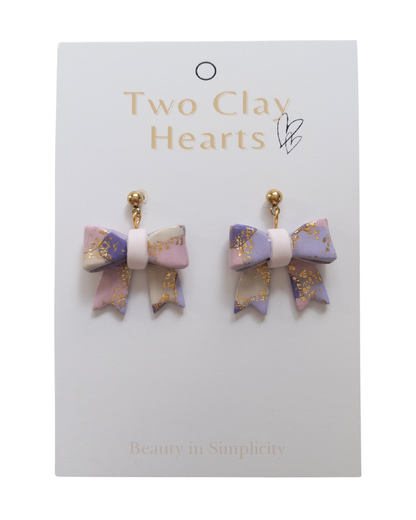 Pair of bow-shaped earrings on a 'Two Clay Hearts' branded card.