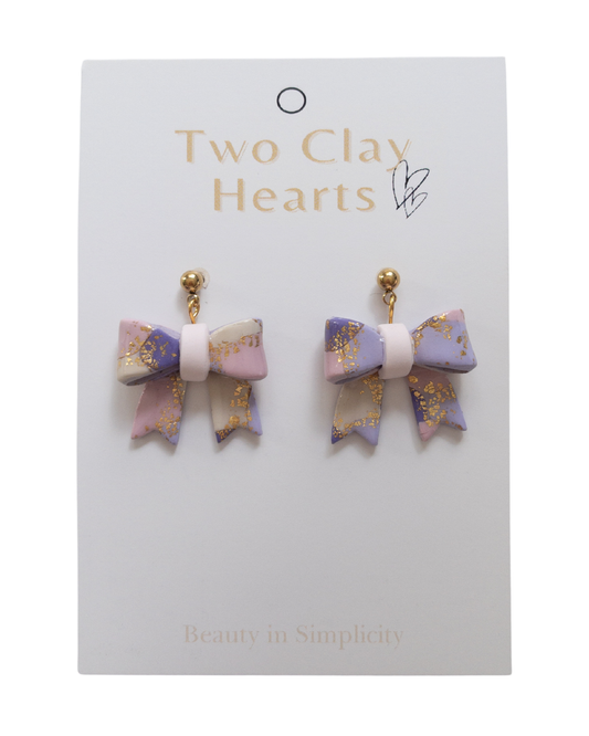 Pair of bow-shaped earrings on a 'Two Clay Hearts' branded card.