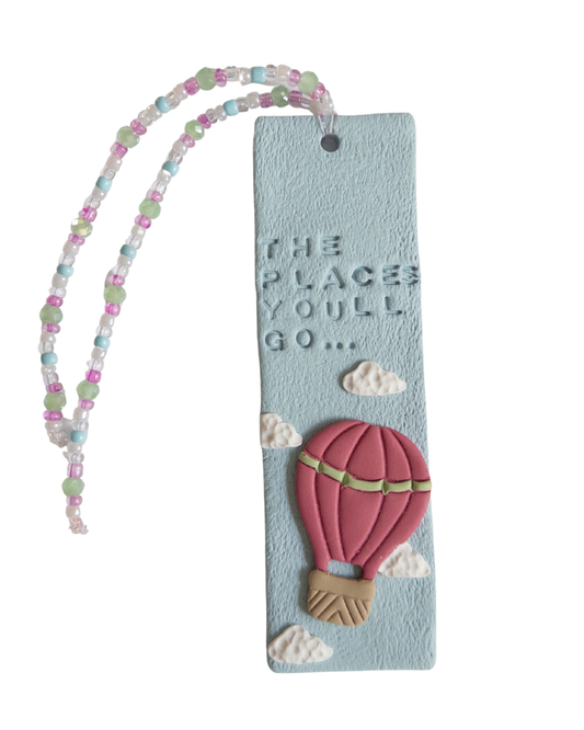 Polymer clay bookmark and matching beaded tassel on white background. Bookmark features words 'the places you'll go' on a blue background, with white clouds and a pink hot air balloon.