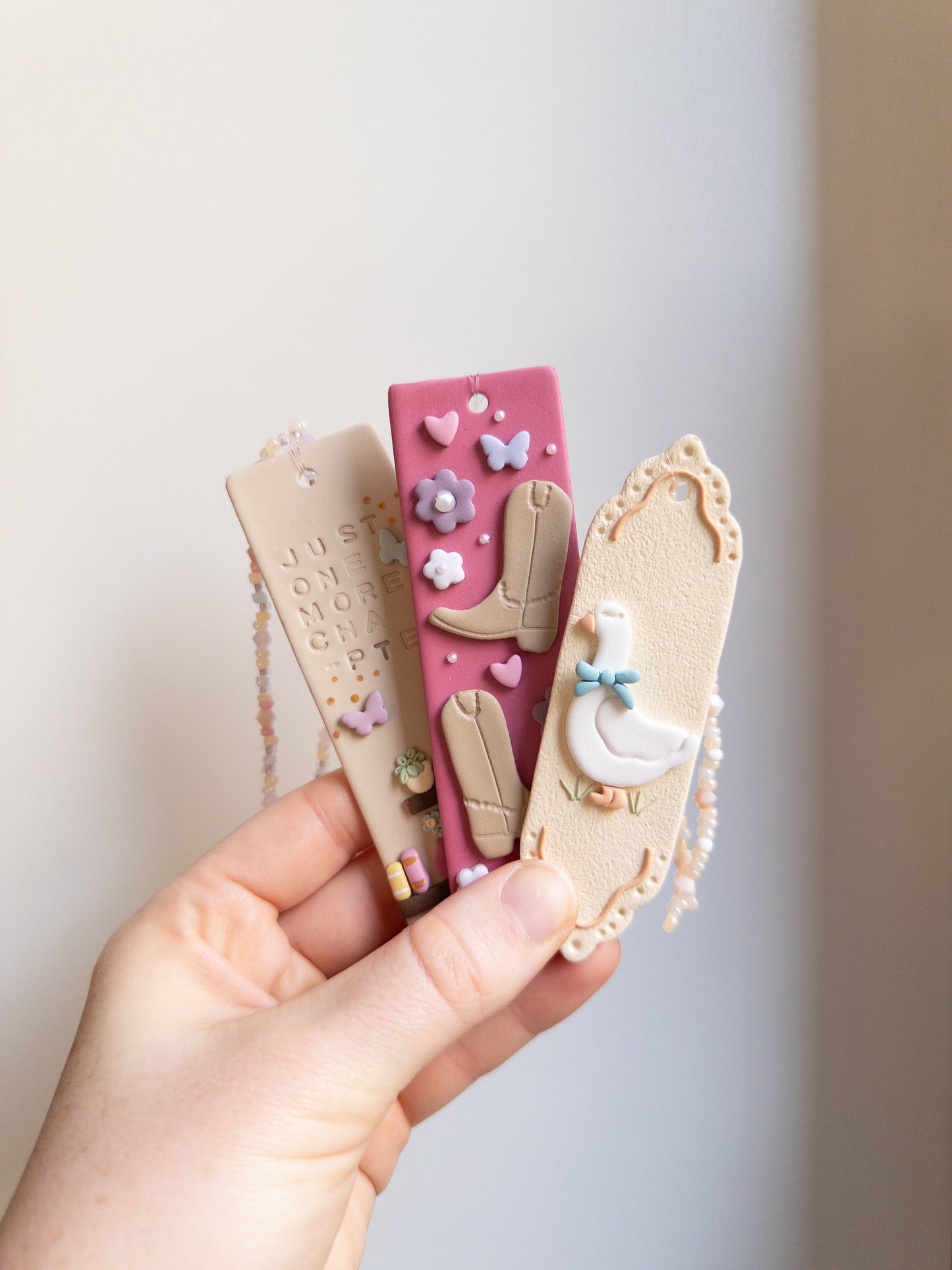 Different designs of polymer clay bookmarks in pastel colours held in someone's hand
