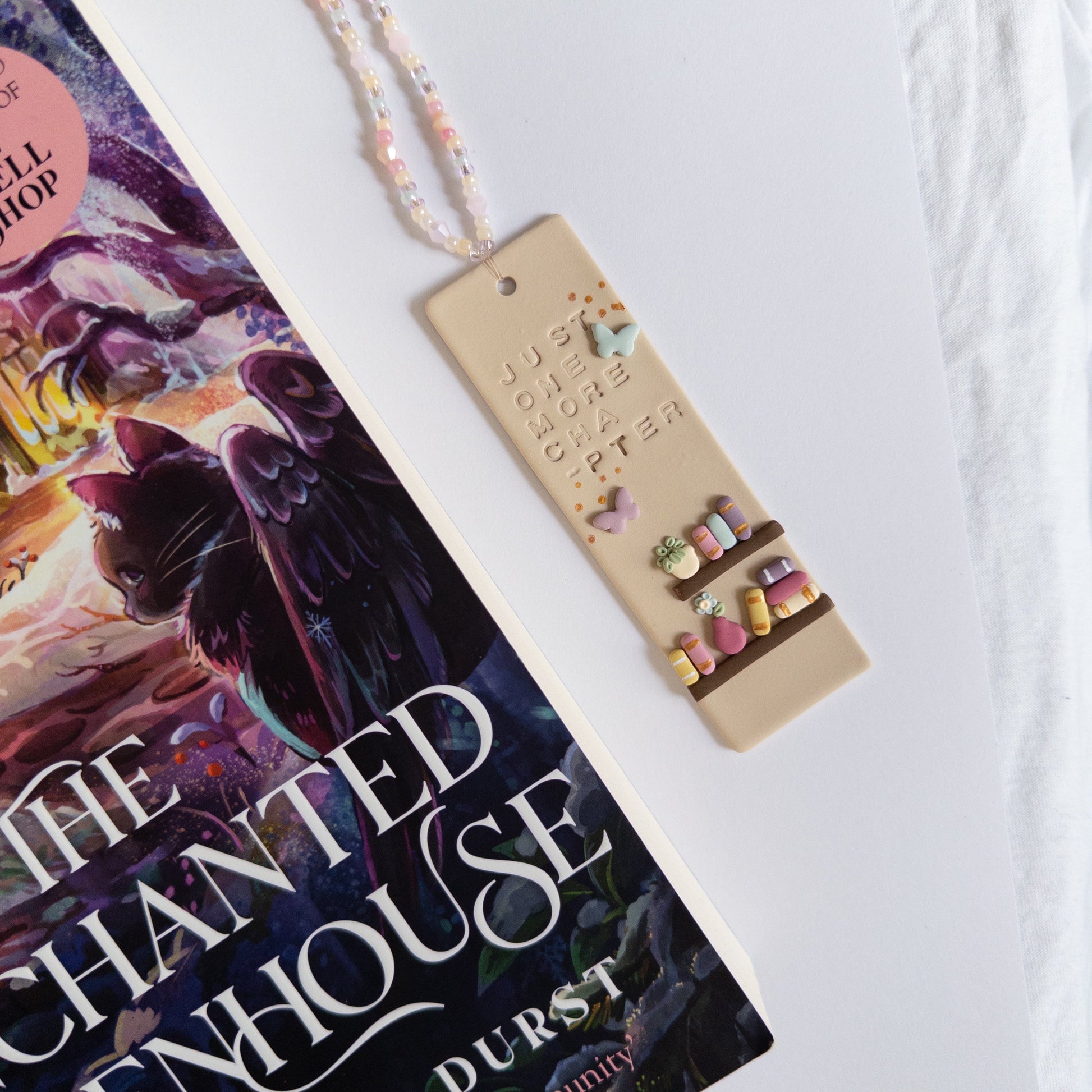 Polymer clay bookmark with beaded tassel next to reading book on white background