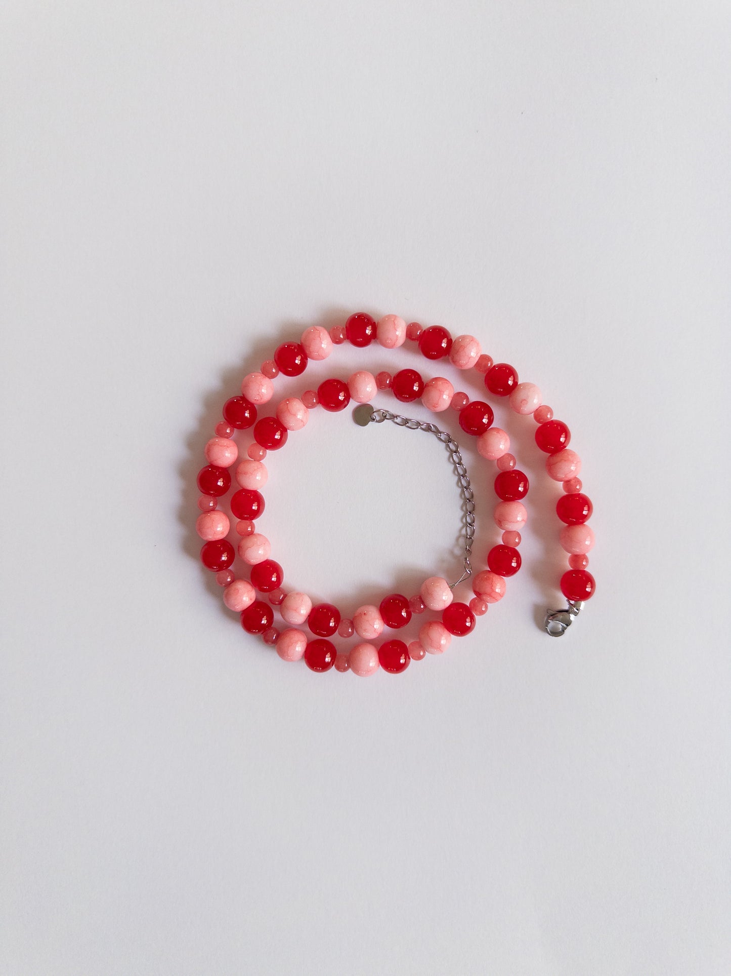 Red and Pink beaded necklace with stainless silver extender styled on a plain whitebakground