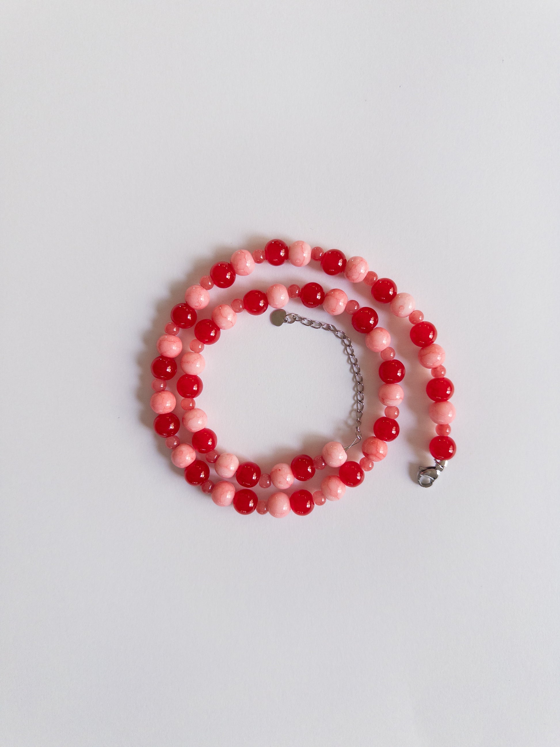 Red and Pink beaded necklace with stainless silver extender styled on a plain whitebakground