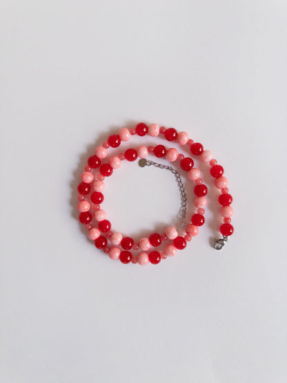 Red and Pink beaded necklace with stainless silver extender styled on a plain whitebakground