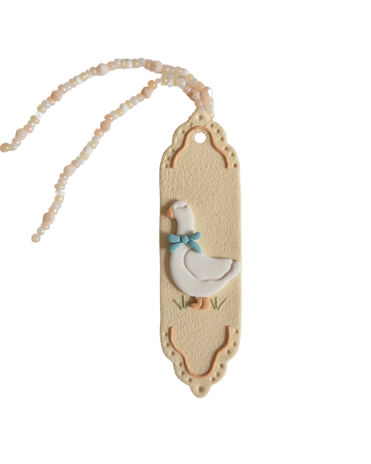 Beige coloured polymer clay bookmark with a white goose on it and a beige and white beaded tassel