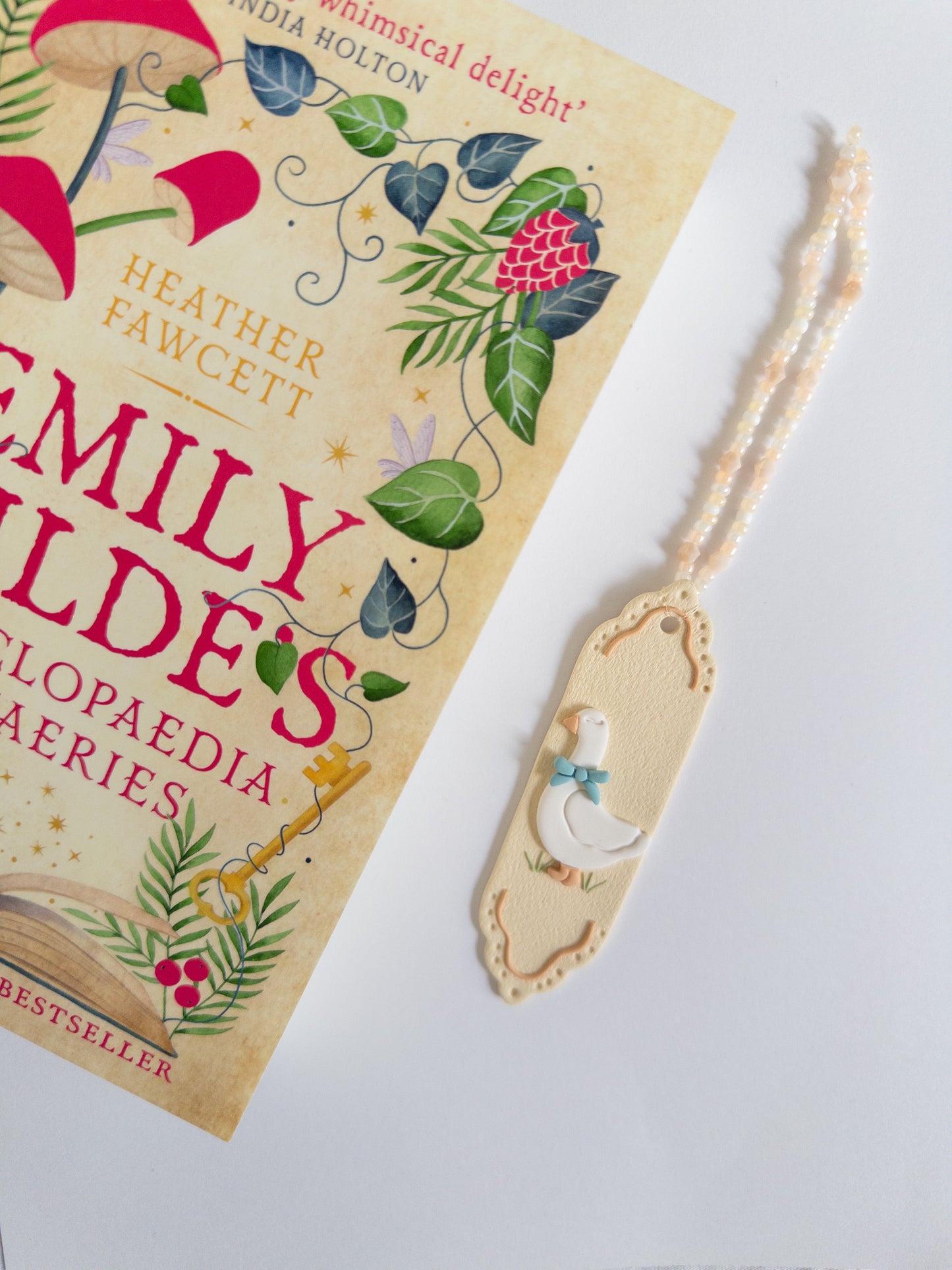 Silly Goose Polymer clay bookmark on a white background, next to a fantasy book