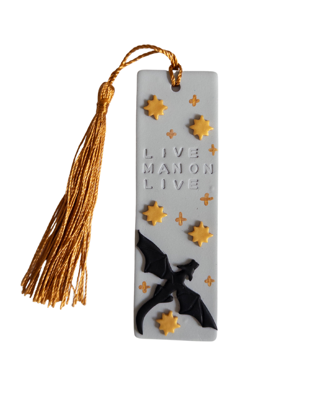 Grey polymer clay bookmark with gold coloured tassel on white background. Bookmark features a dragon, gold stars and the words 'live Manon live'