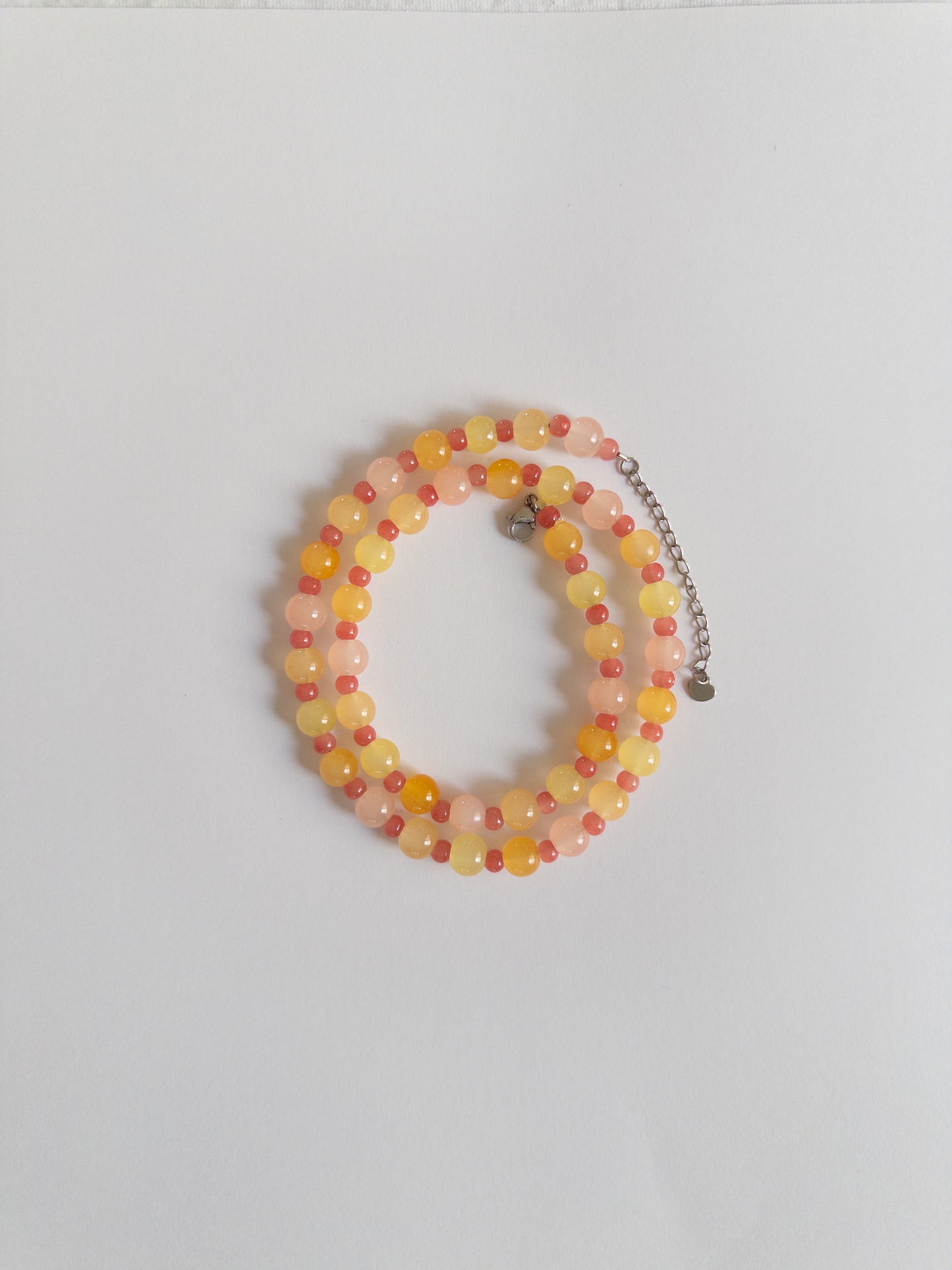 Orange, yellow and pink beaded necklace styled on a white background