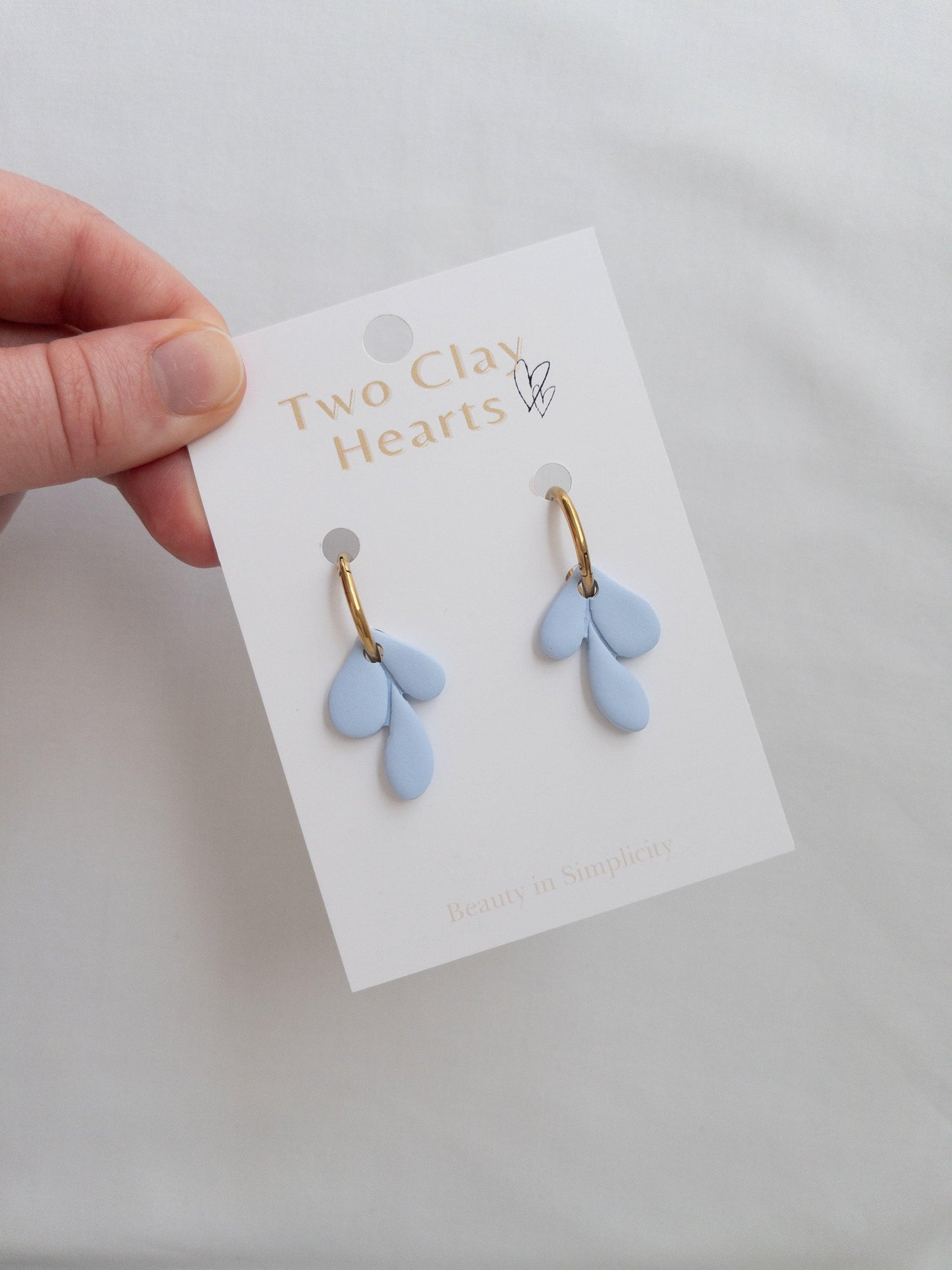 Elegant gold and blue leaf hoop earrings on white backing card