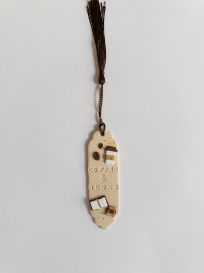 Beige polymer clay bookmark with brown tassel on white background. Bookmark features the words 'coffee & books' and decals of a coffee cup, coffee beans and books.
