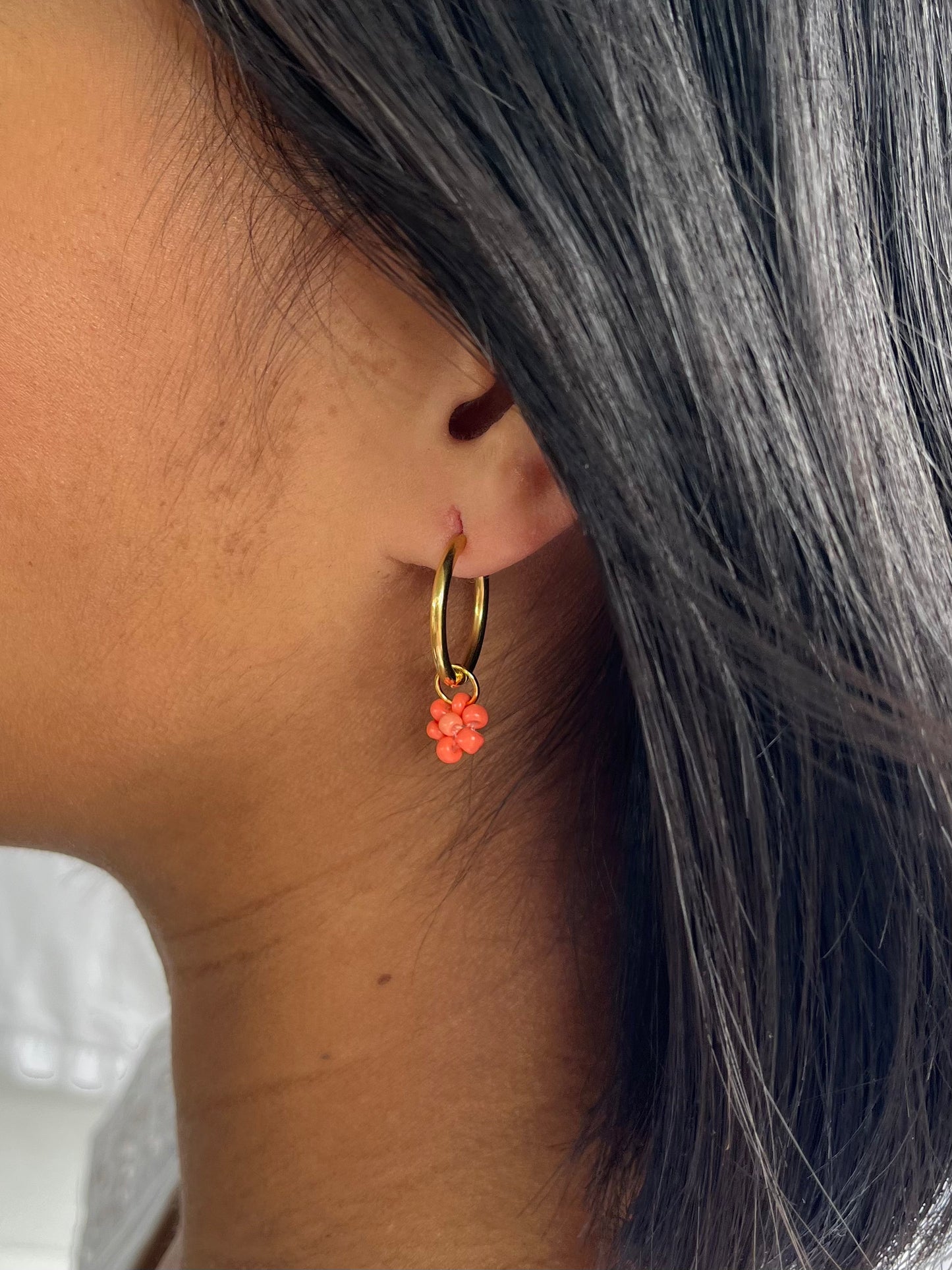 Close up on gold hoops with coral beaded flowers on models ear