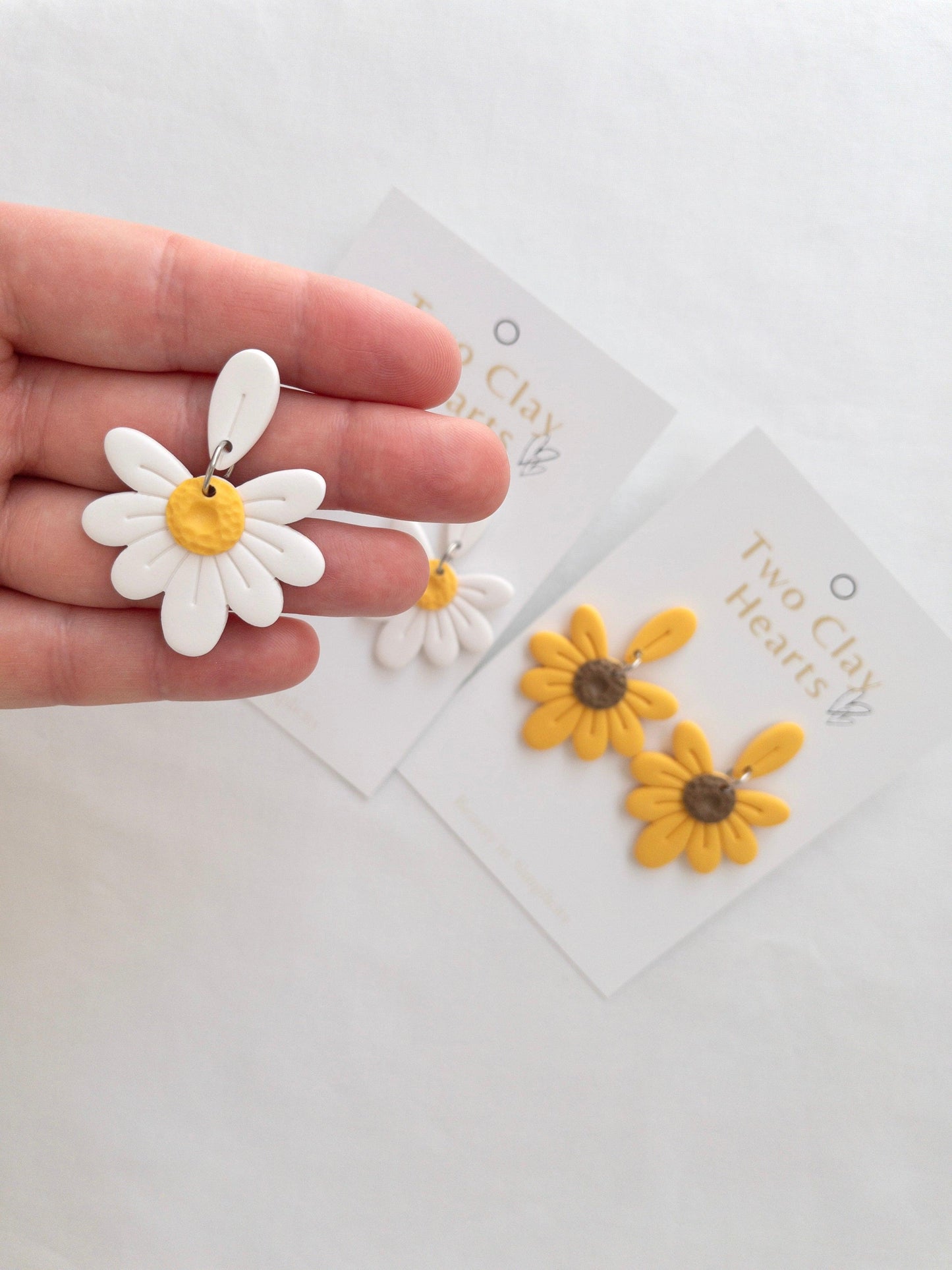 white daisy earrings with yellow centre held in a modals hand