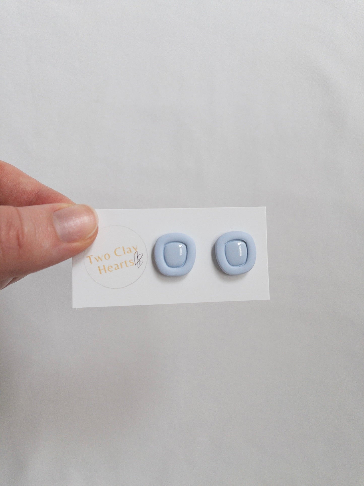 Blue polymer clay stud earrings with a resin centre, on a white backing card