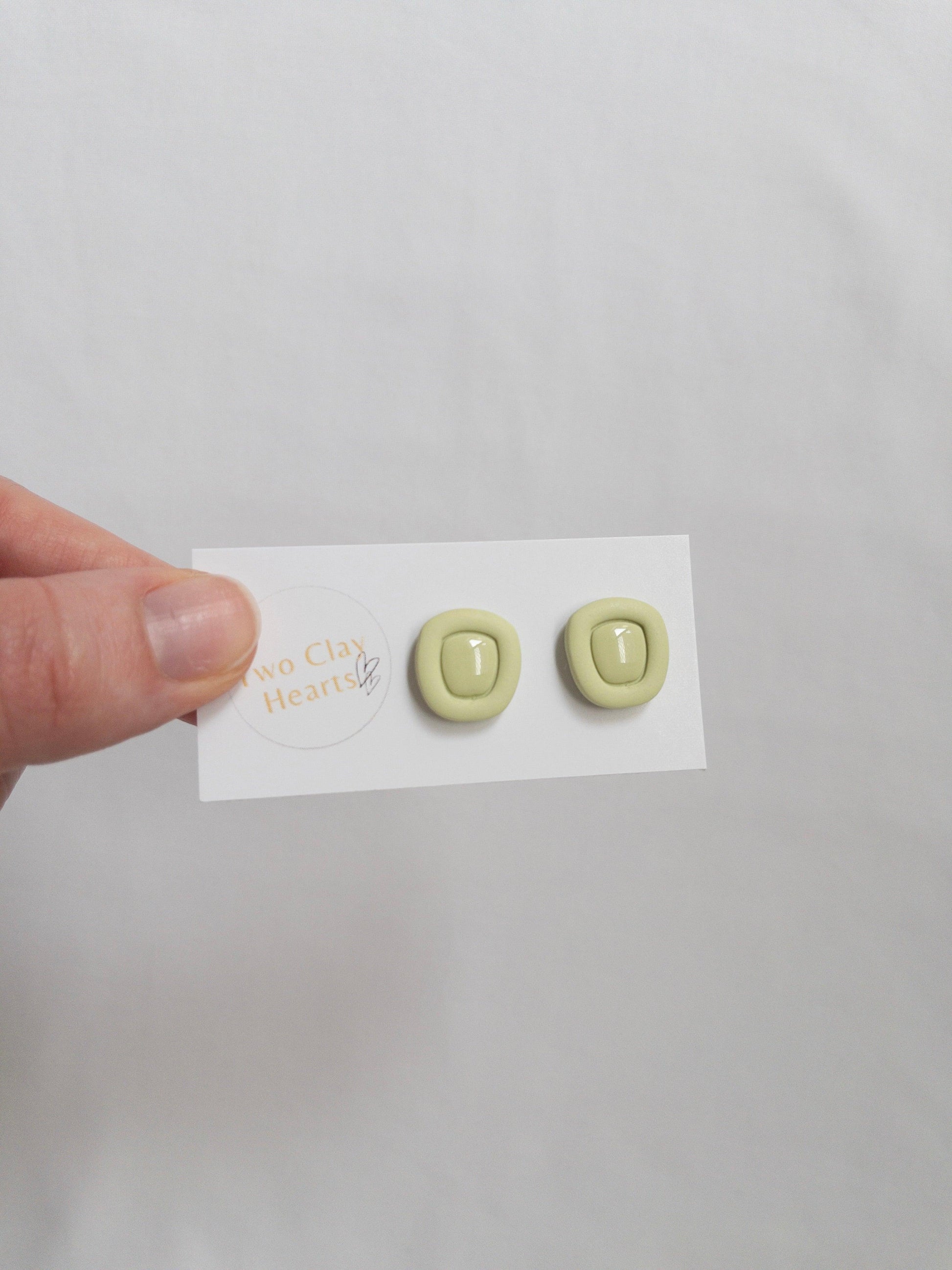 Green polymer clay stud earrings with a resin centre, on a white backing card