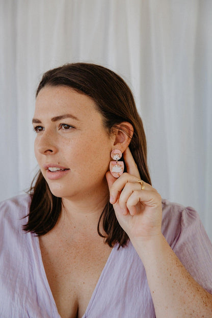 Orange, gold and maroon patterned, half oval dangle earrings worn on a models ear