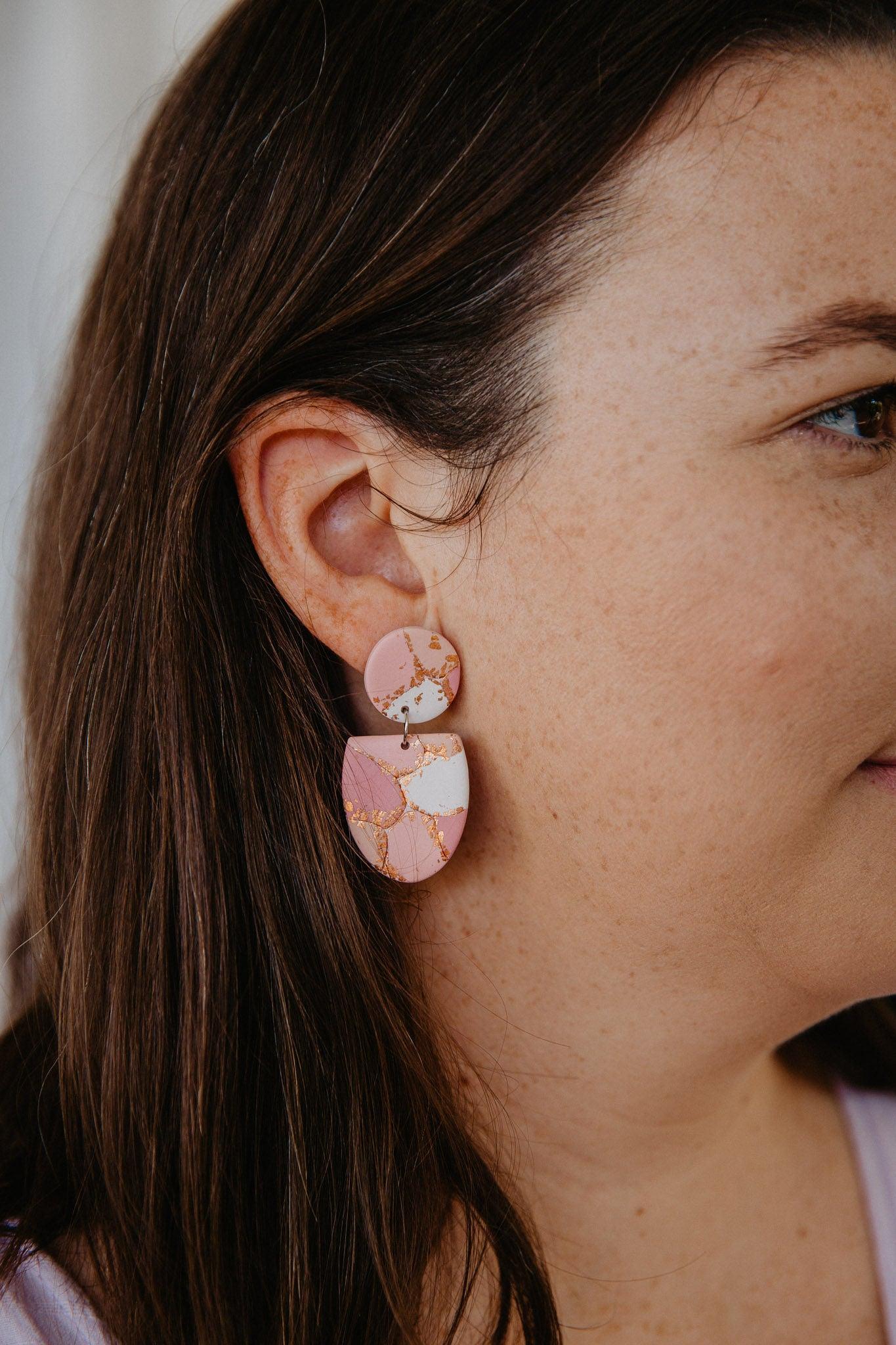 Orange, gold and maroon patterned, half oval dangle earrings worn on a models ear