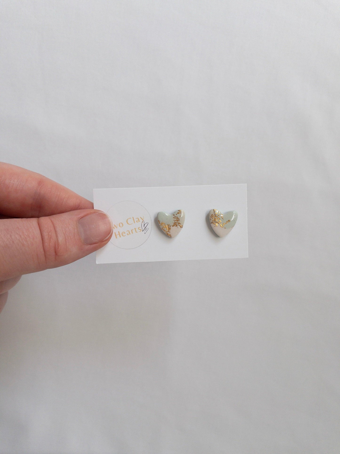 Green and gold heart shaped stud earrings on white backing card