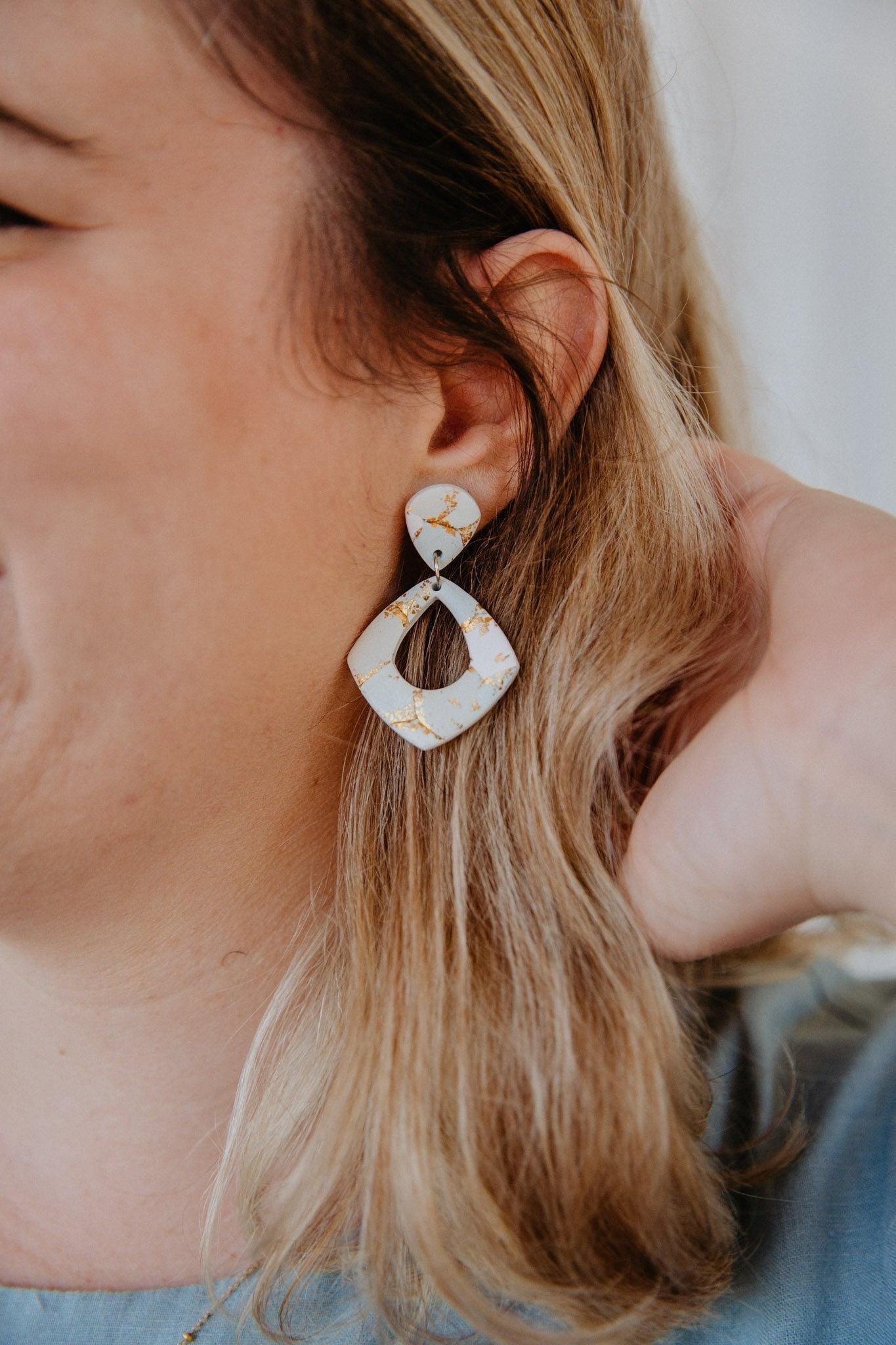 diamond shape gold patterned dangle earring worn on a model's ear.