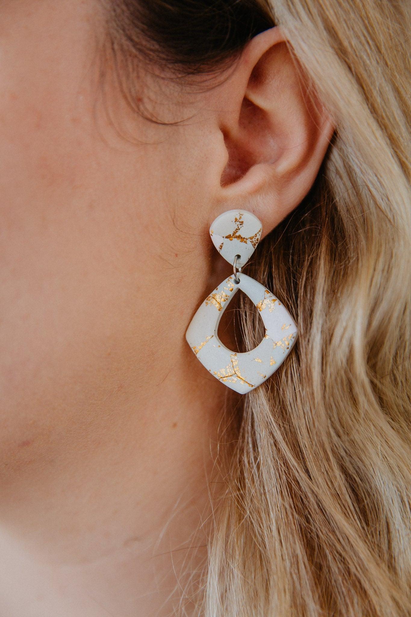 close up on diamond shape gold patterned dangle earring worn on a model's ear.