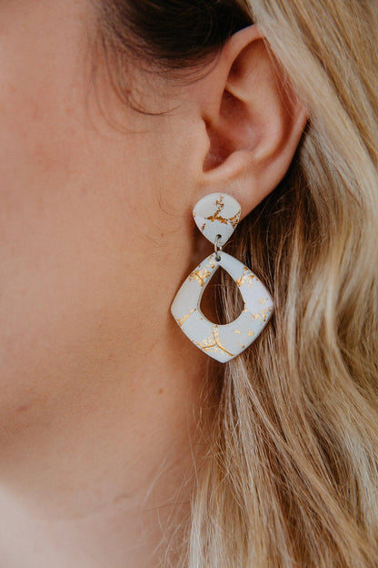 close up on diamond shape gold patterned dangle earring worn on a model's ear.