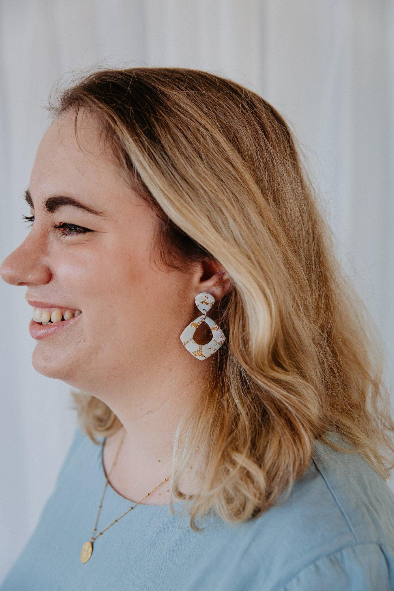 diamond shape gold patterned dangle earring worn on a model's ear.