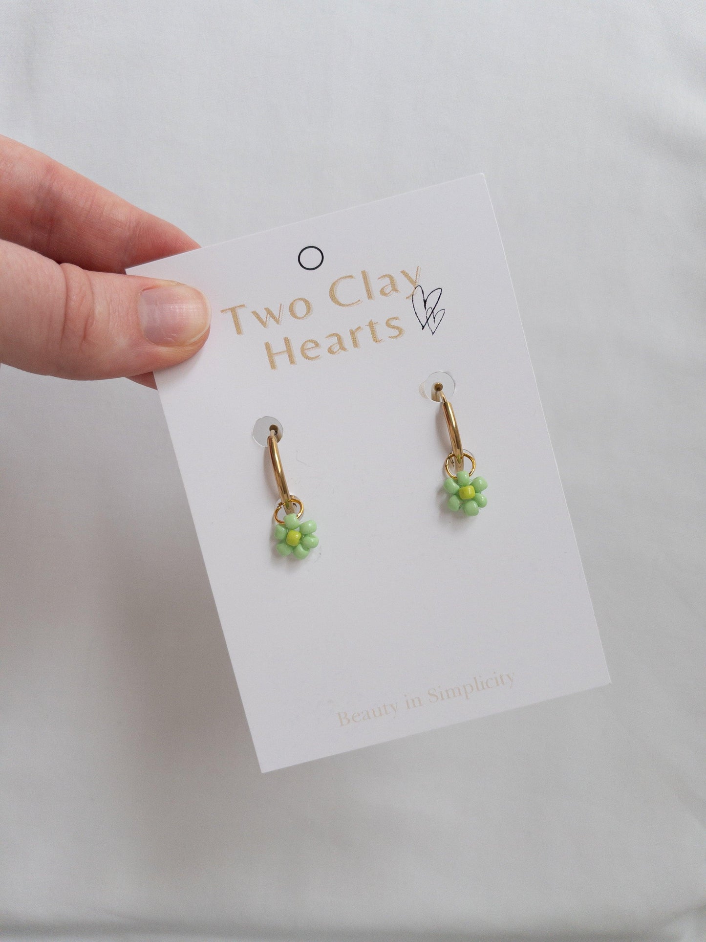 Gold hoops with green beaded flowers on white backing card