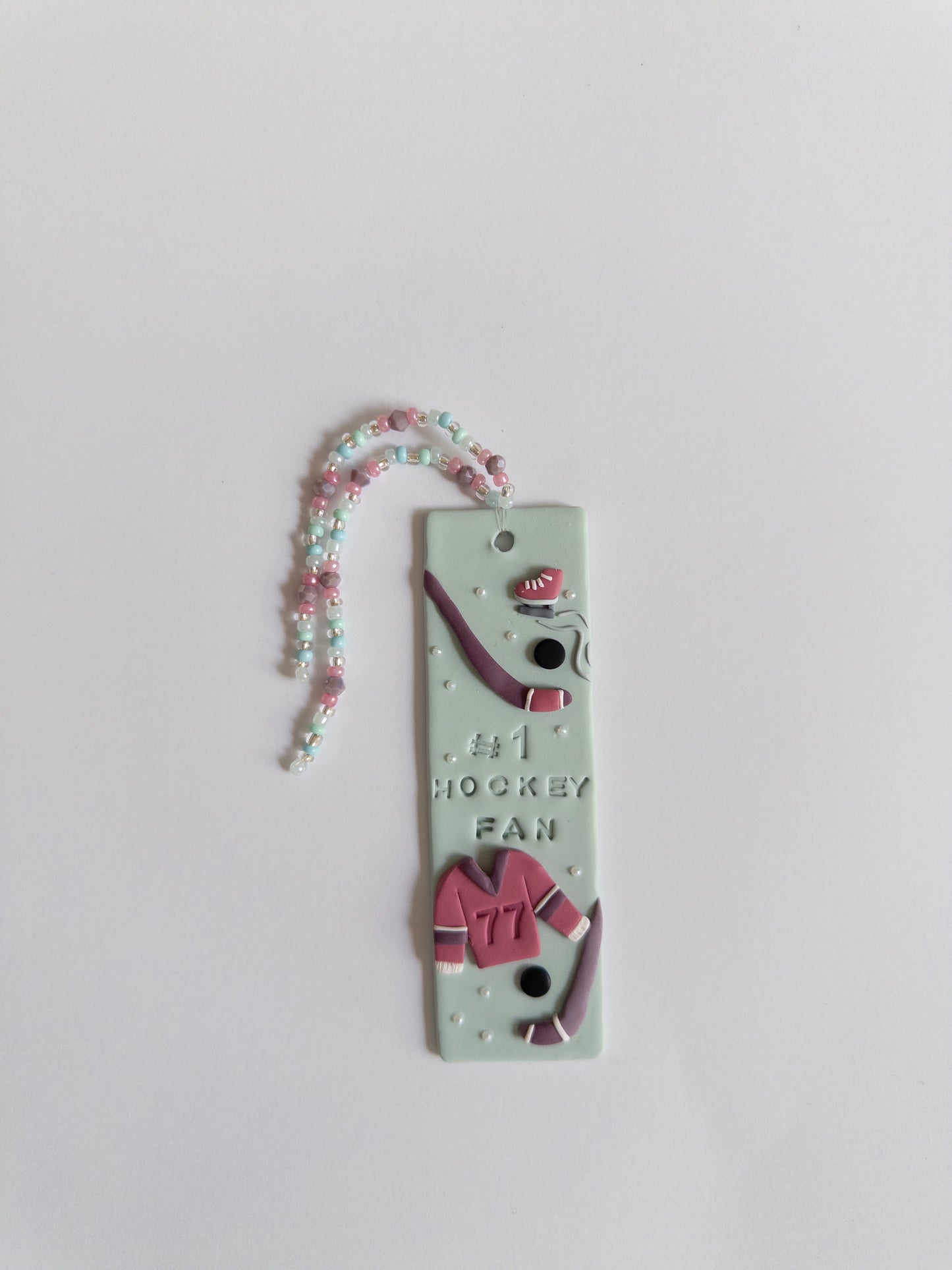 Polymer clay bookmark and matching beaded tassel on white background. Bookmark features a design with the words '#1 Hockey Fan" and hockey sticks and jersey design details