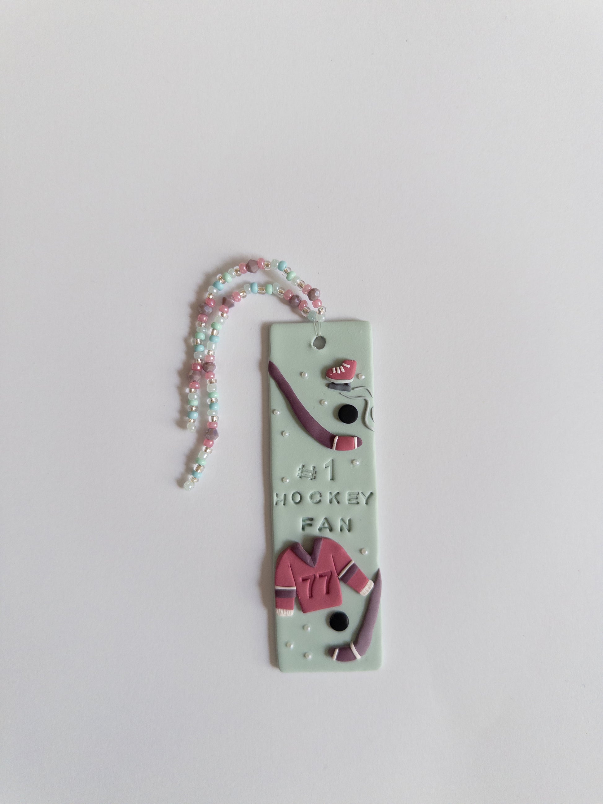 Polymer clay bookmark and matching beaded tassel on white background. Bookmark features a design with the words '#1 Hockey Fan" and hockey sticks and jersey design details