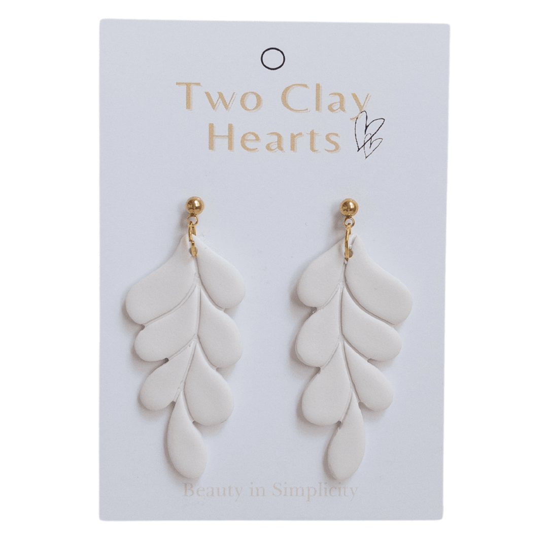 Clos up of white and gold leaf dangle earrings on white backing card