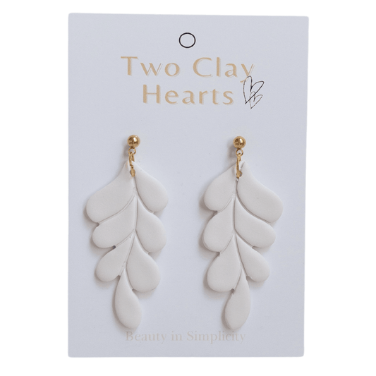 Clos up of white and gold leaf dangle earrings on white backing card